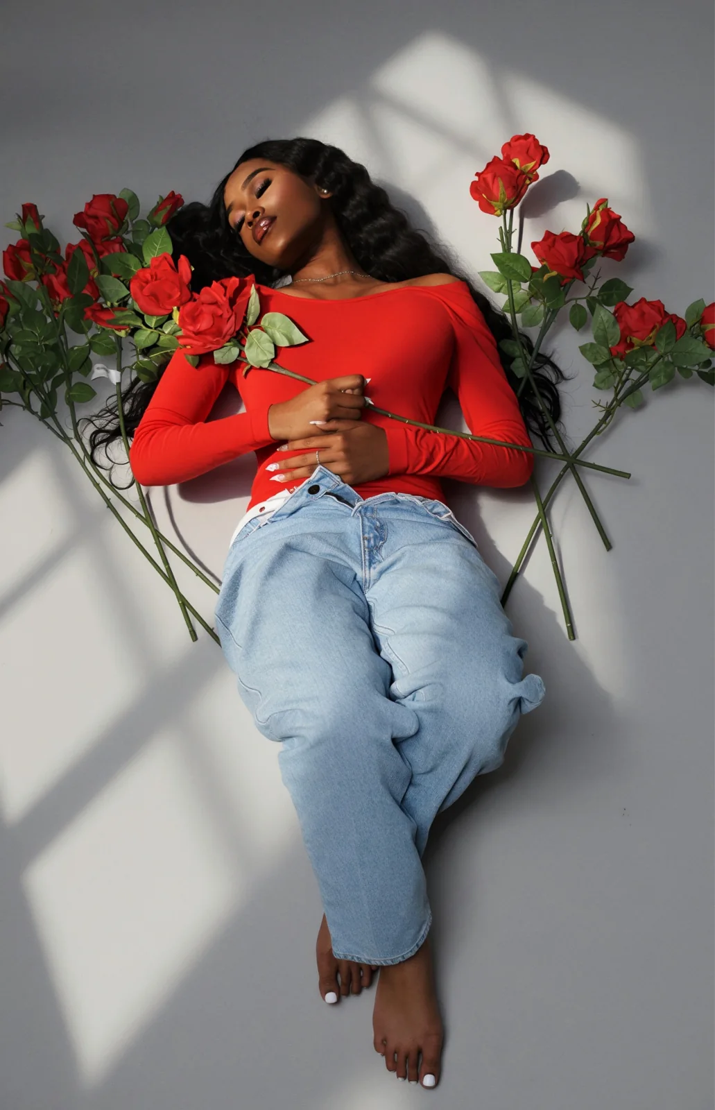 Red top and light-wash jeans laid flat with scattered long-stemmed roses