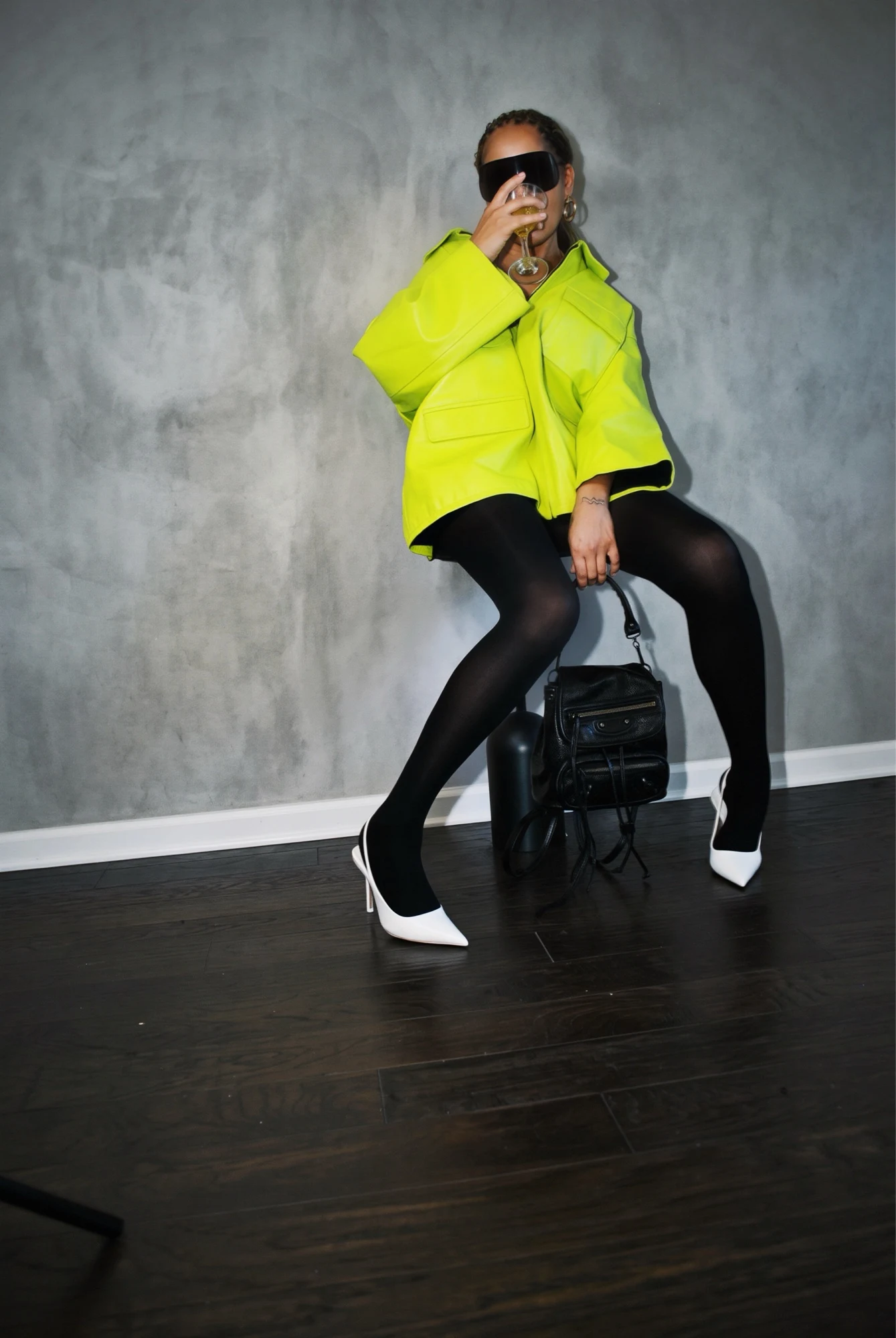 Neon chartreuse leather jacket with visor sunglasses, seated with a coupe glass